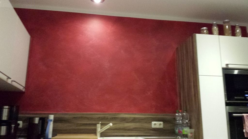 Rote strukturierte Küchenwand mit weißen Schränken und Akzentbeleuchtung.