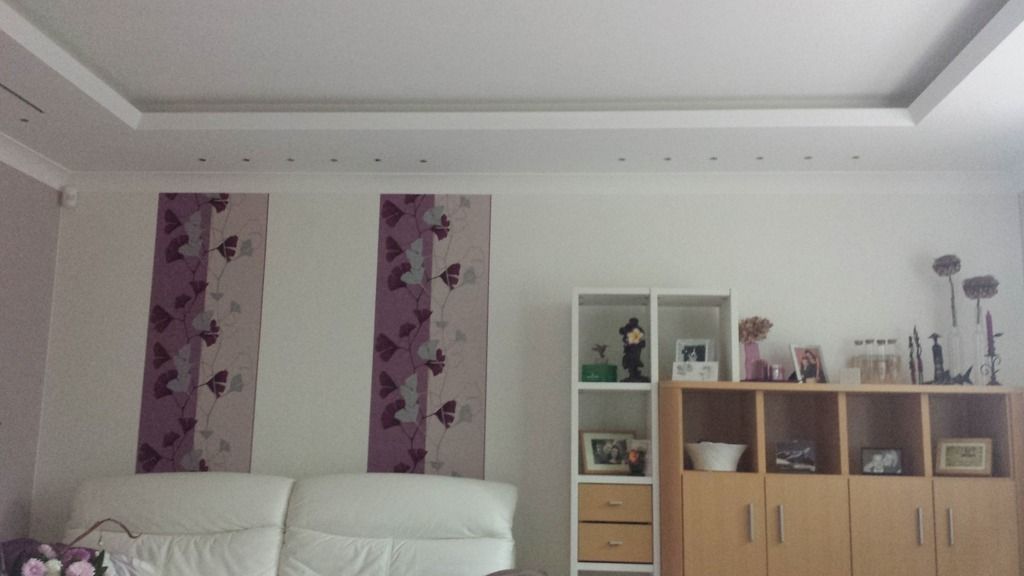 Wohnzimmer mit weißen Wänden, weißem Sofa, lila Schmetterlingsvorhängen und einem Holzschrank.