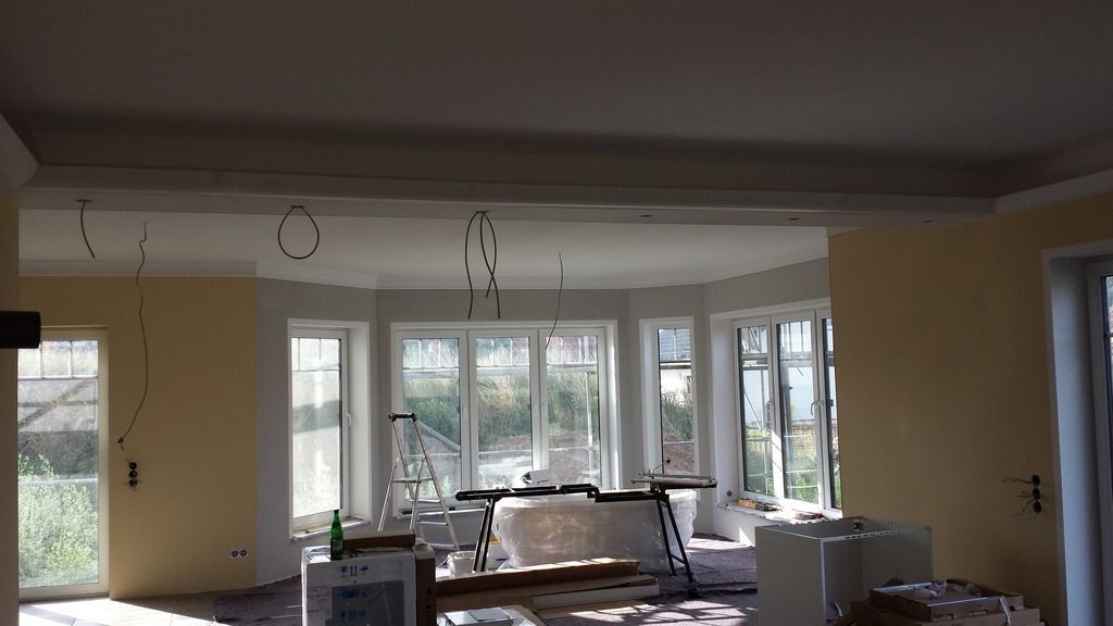 Innenansicht eines im Umbau befindlichen Raumes mit großen Fenstern, unfertigen Wänden und hängenden Kabeln.