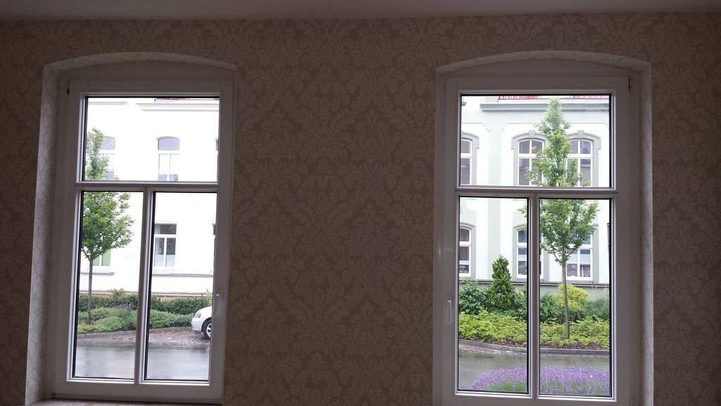 Zwei weiß gerahmte Fenster mit Blick auf ein Gebäude und die Landschaft, ein Fenster teilweise geöffnet.