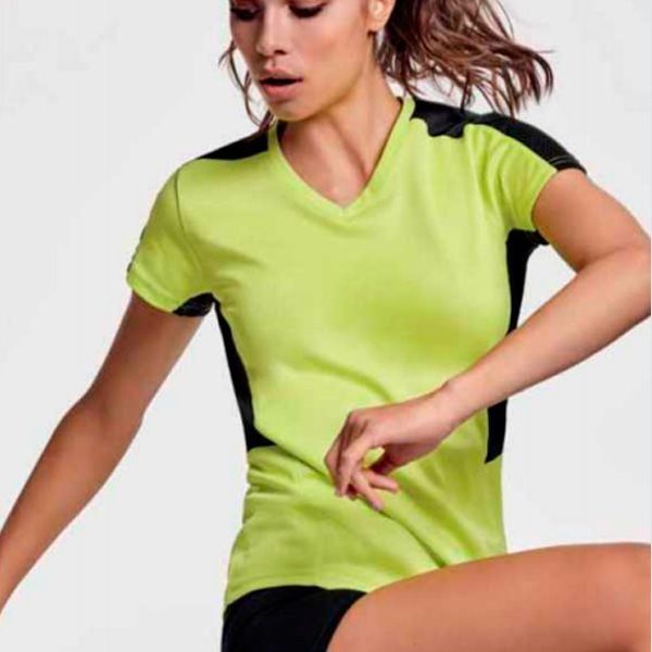 Una mujer lleva una camiseta de color amarillo neón y pantalones cortos negros.