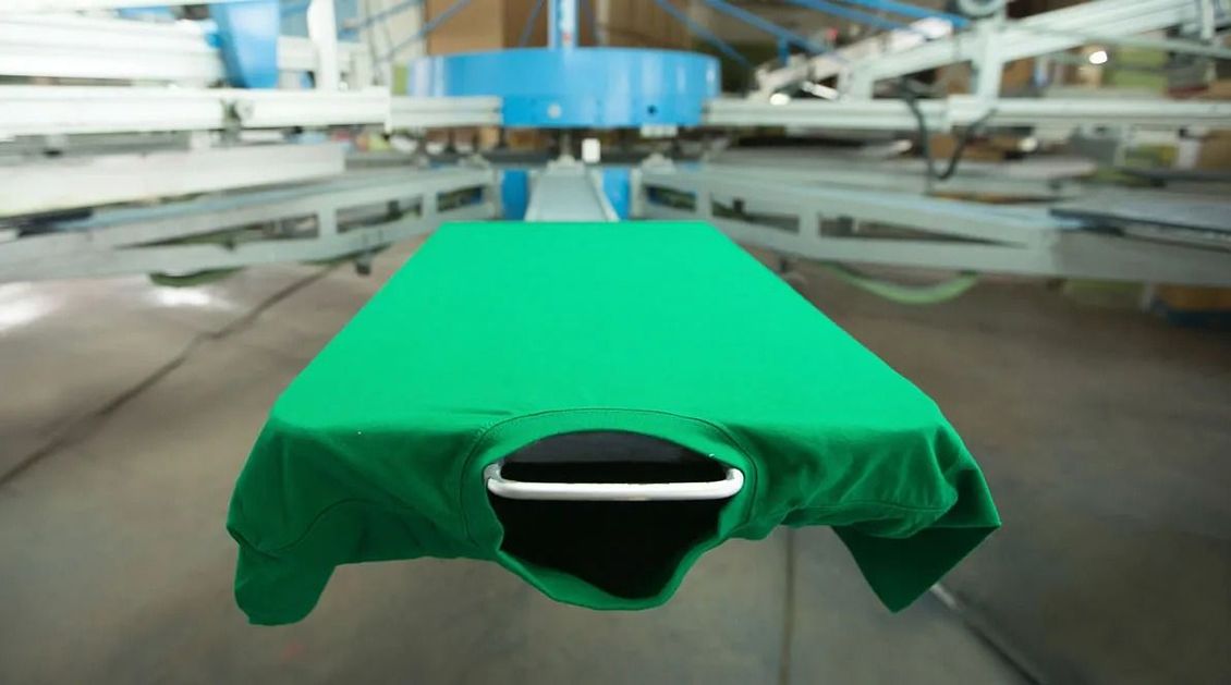 Se está imprimiendo una camiseta verde en una máquina en una fábrica.