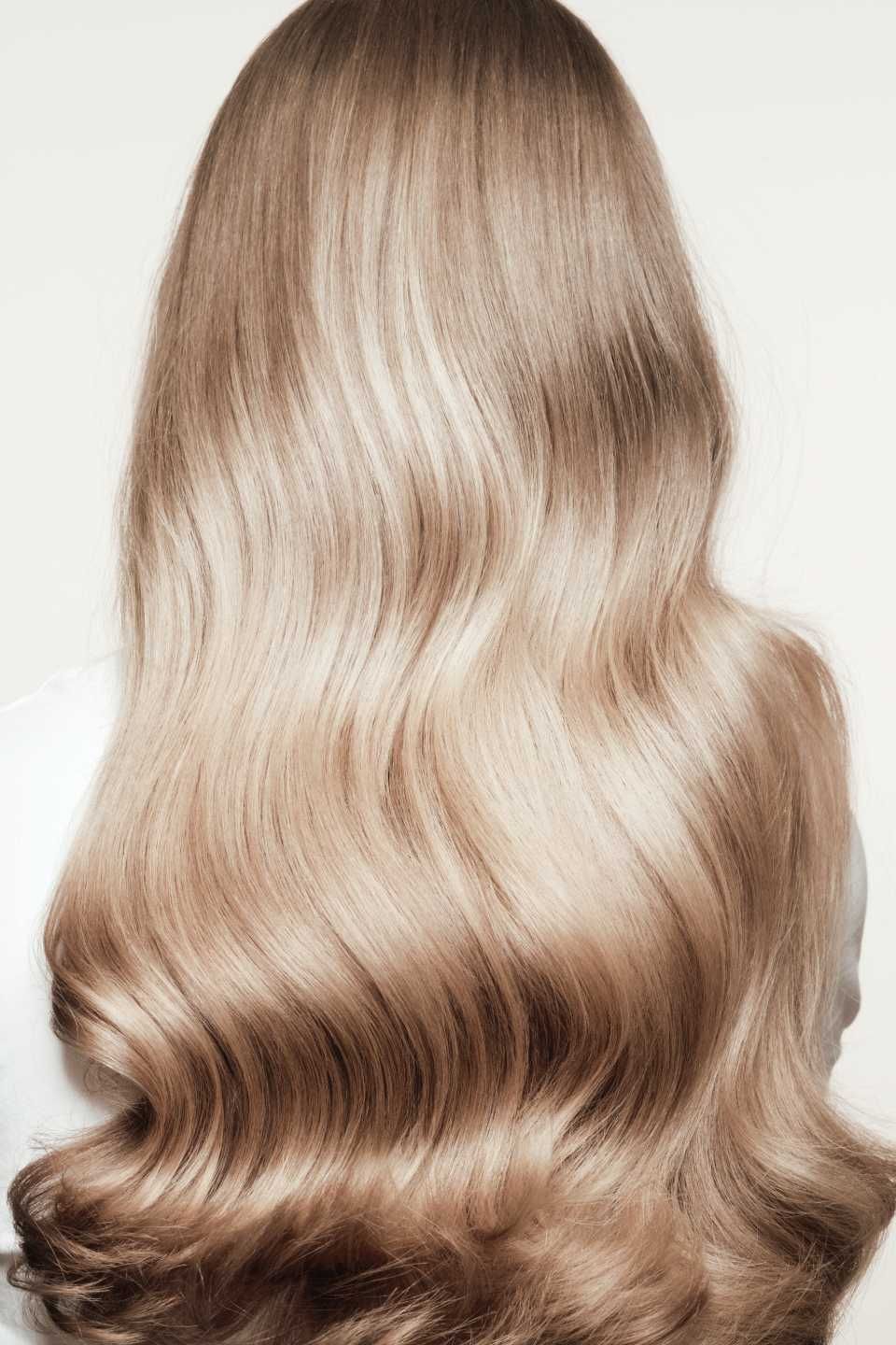 Langes, gewelltes blondes Haar vor weissem Hintergrund.