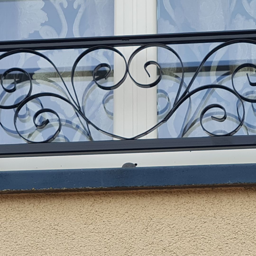 Rampe en bois blanc avec barreaux métalliques horizontaux, donnant sur une forêt.