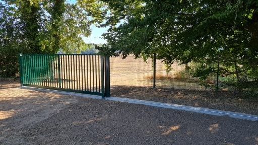 Un ouvrier en costume gris et gants installe une barrière métallique ; gros plan.
