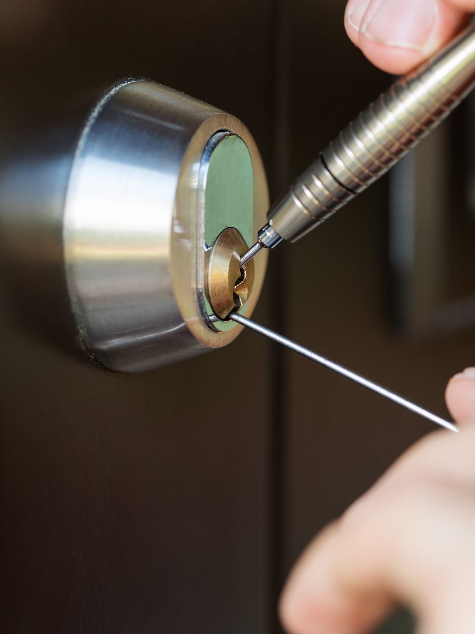 Gros plan d'une personne crochetant une serrure de porte avec deux outils métalliques.