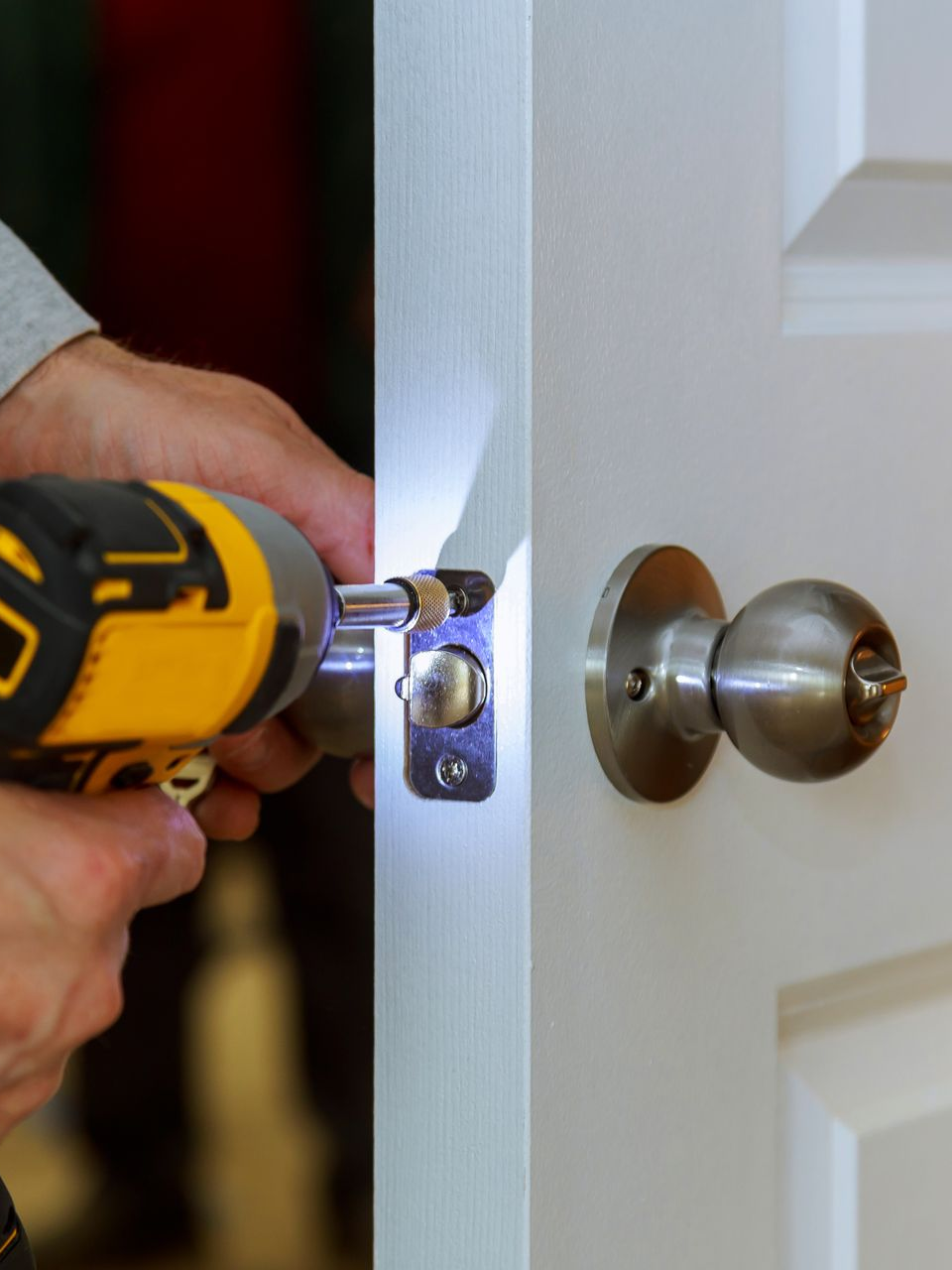 Personne installant une poignée de porte avec une perceuse électrique jaune et noire sur une porte blanche.