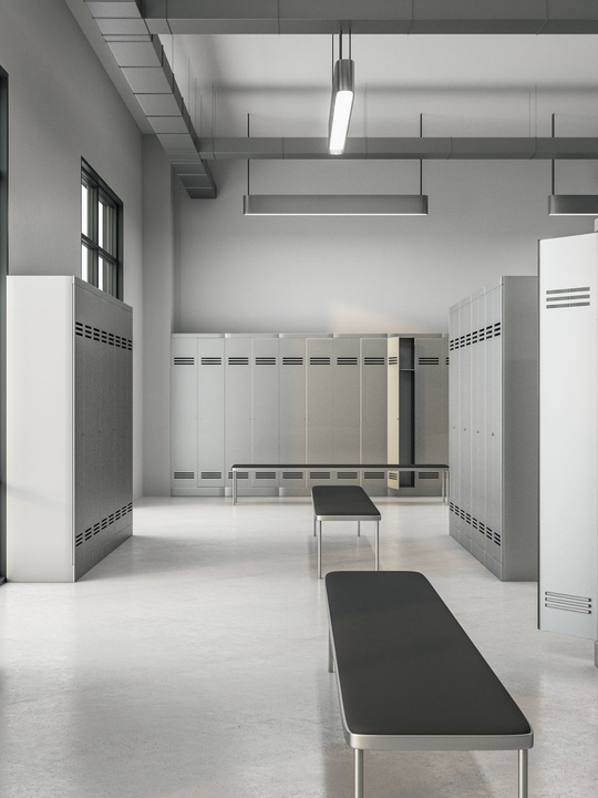 Vestiaire vide avec des rangées de casiers gris, des bancs et un éclairage vif.