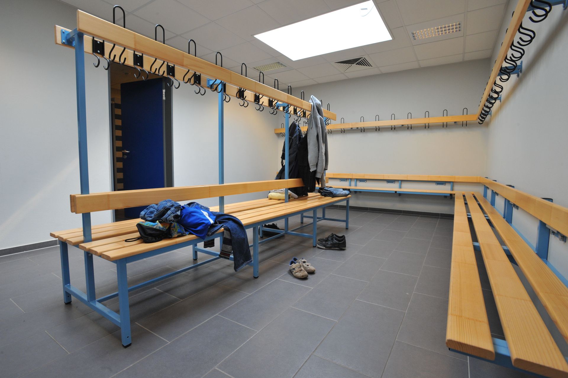 Vestiaire vide avec bancs en bois et vêtements suspendus.