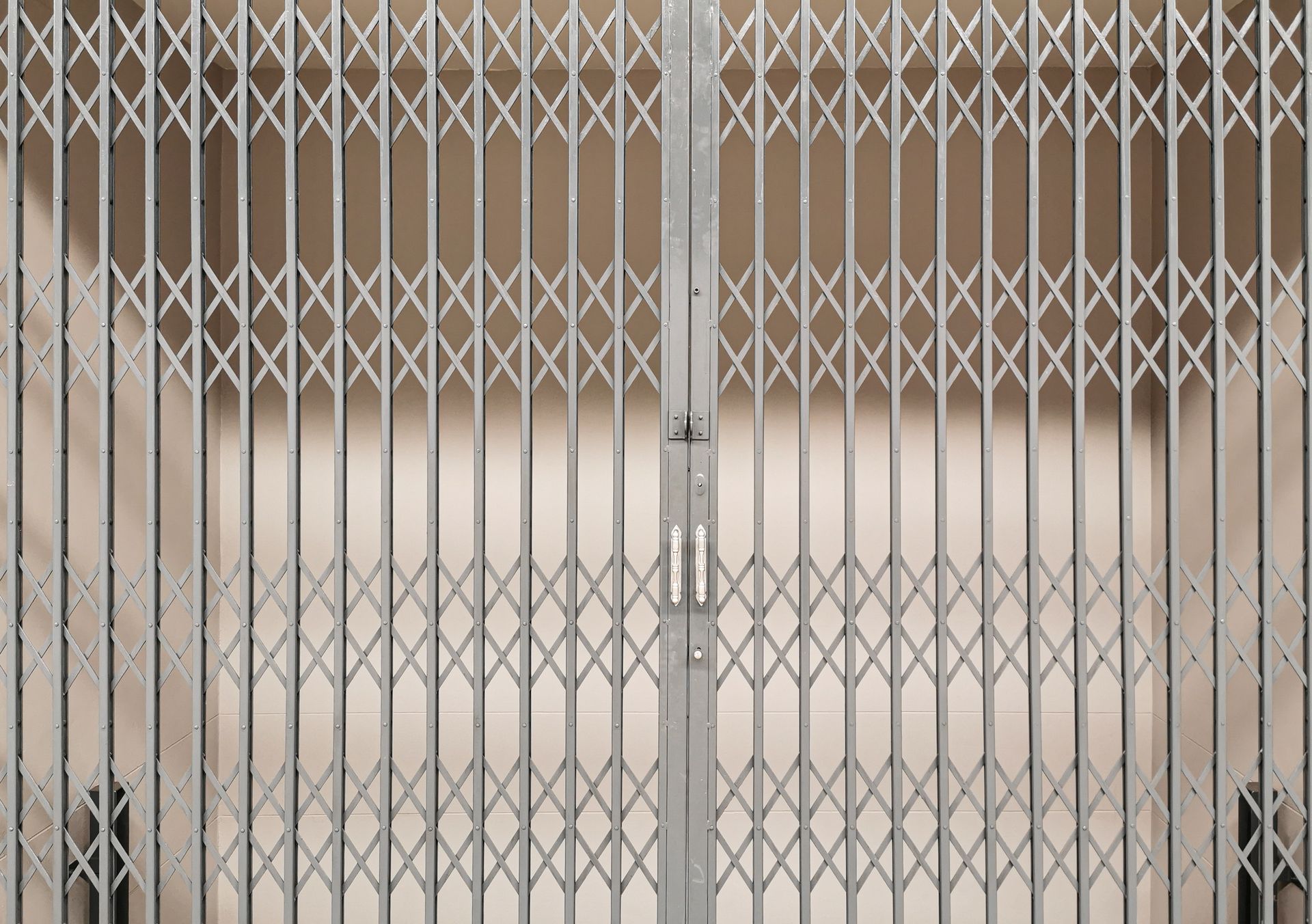 Portail de sécurité en métal argenté fermé contre un mur beige.