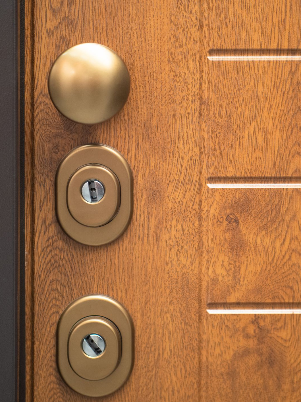 Gros plan d'une porte en bois avec un bouton doré, deux serrures à clé et des rainures horizontales.