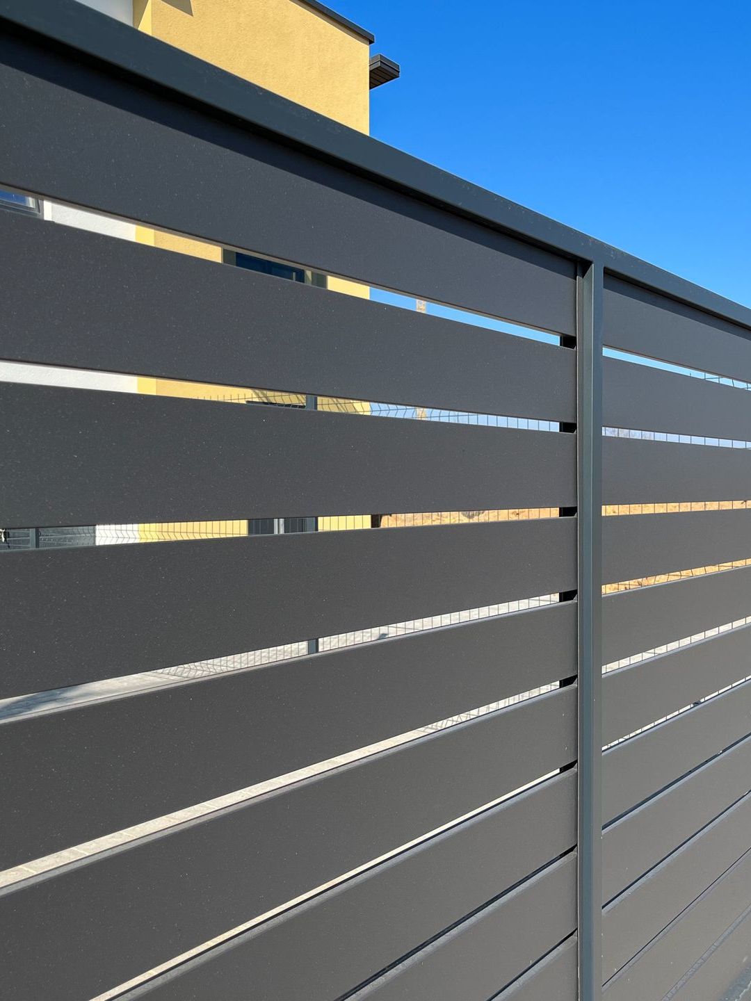 Clôture à lattes horizontales grises avec un fond de ciel bleu.