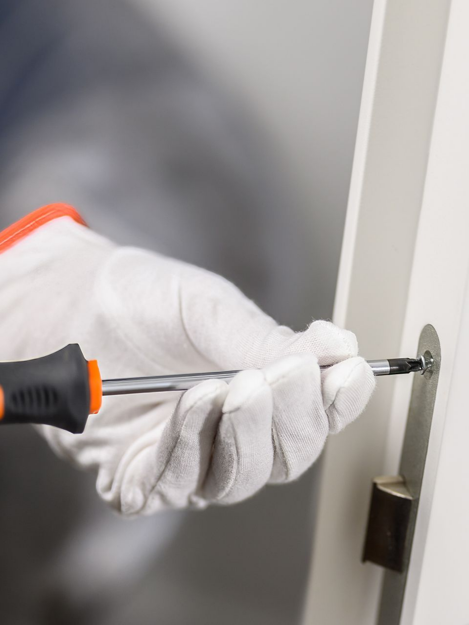 Une personne portant des gants utilise un tournevis pour installer la quincaillerie de porte sur une porte blanche.