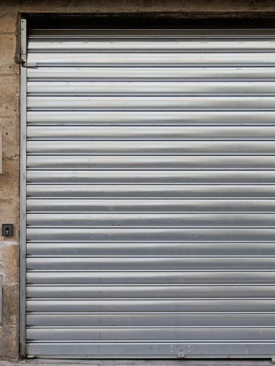Porte roulante en métal gris dans un bâtiment en pierre beige.