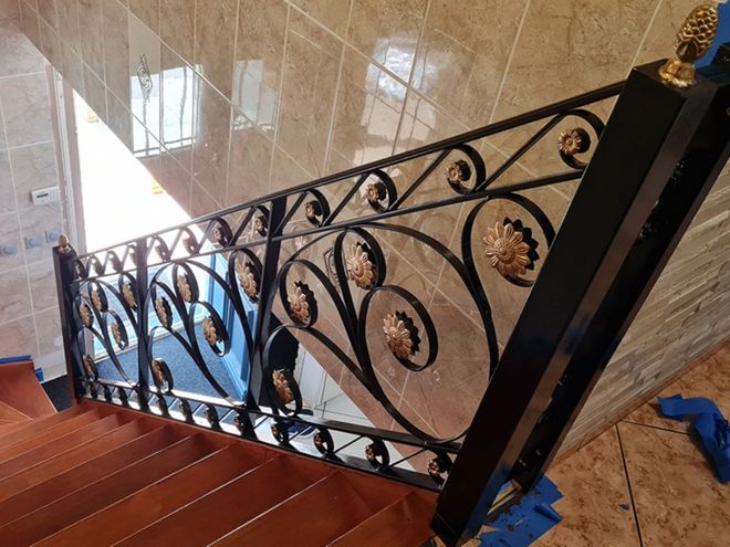 Rampe d'escalier en fer forgé noir et doré avec marches marron.