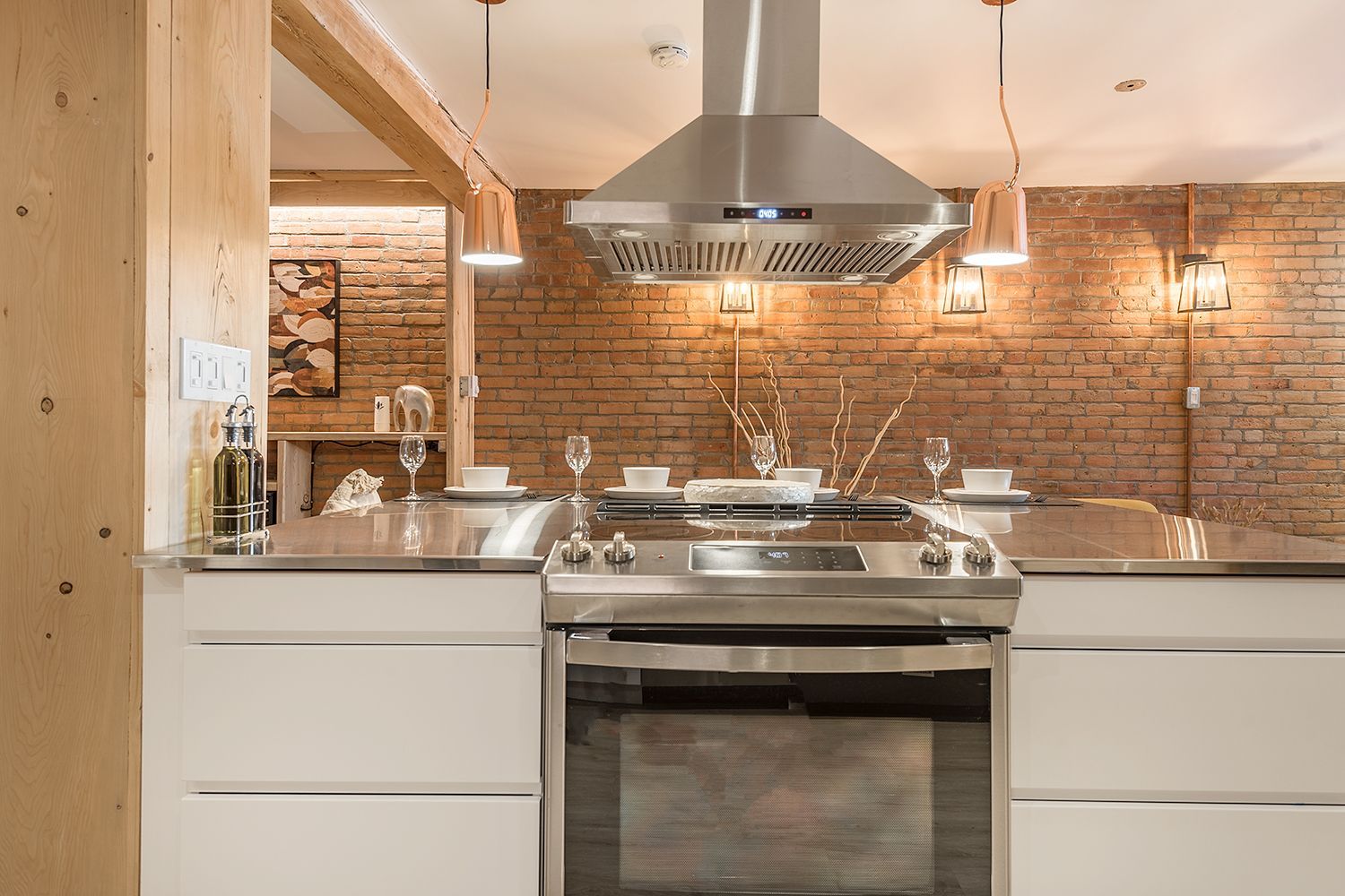 Cuisine moderne avec électroménagers en acier inoxydable, mur de briques, poutres en bois et armoires blanches.