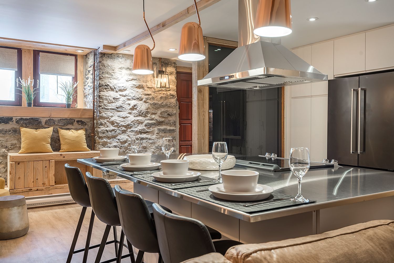 Cuisine moderne avec îlot central, mur en pierre et luminaires métalliques.