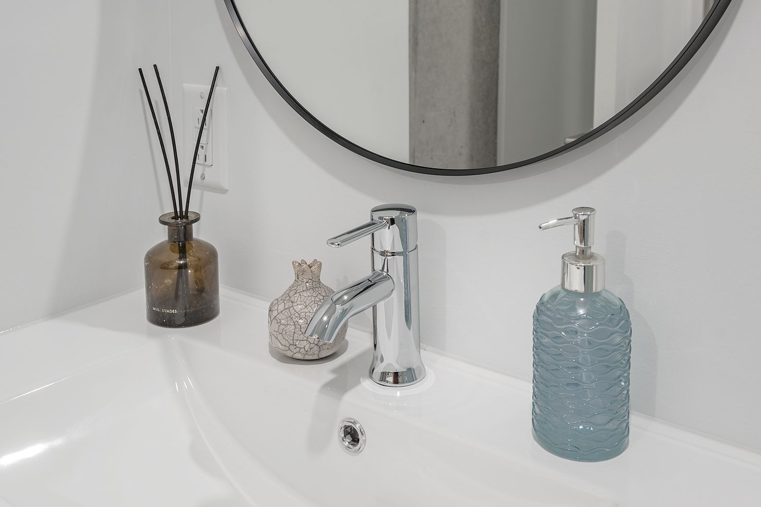 Lavabo de salle de bain avec robinet chromé, miroir rond et bouteilles décoratives.
