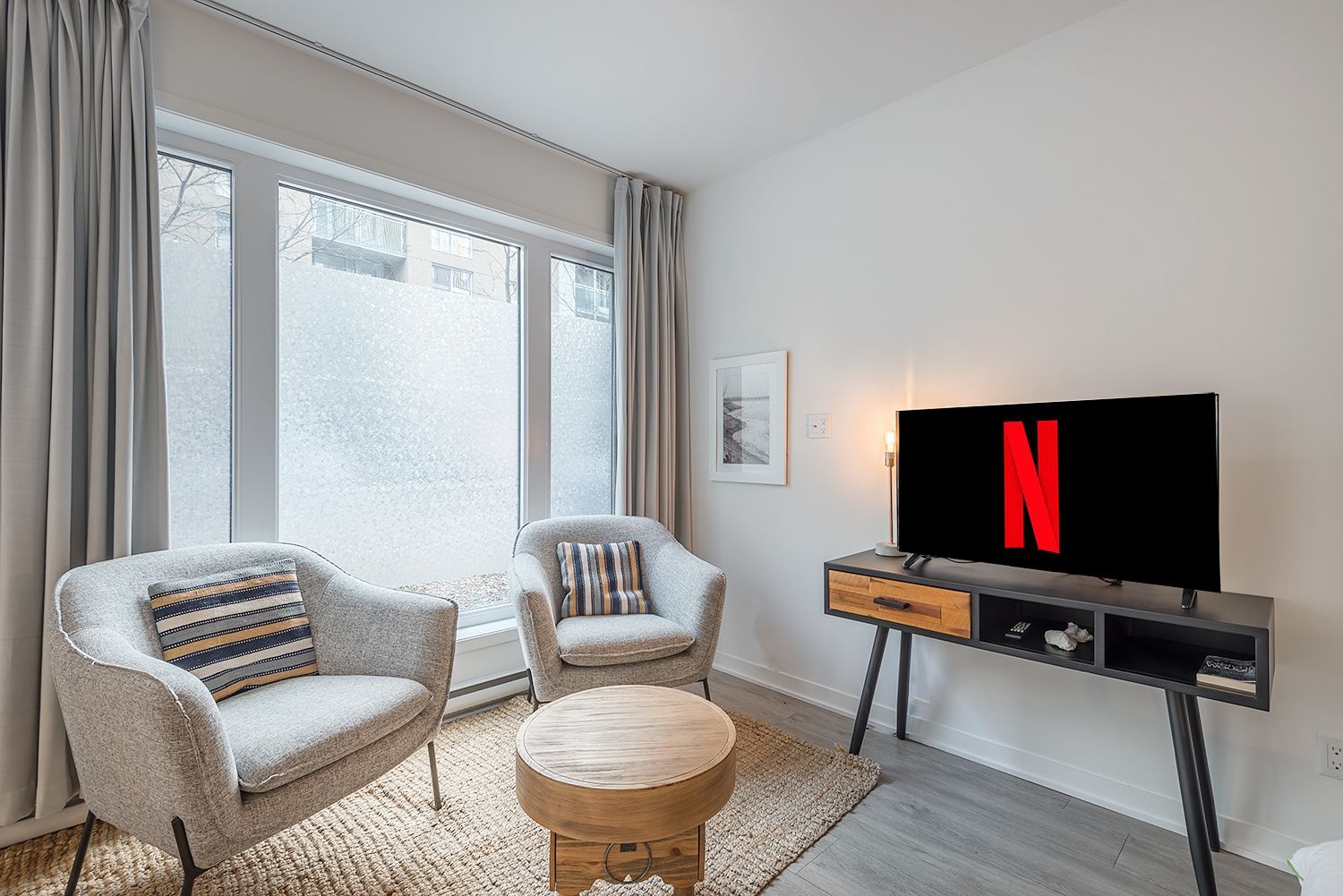 Salon avec deux chaises grises, une petite table en bois, un tapis et une télévision jouant Netflix.