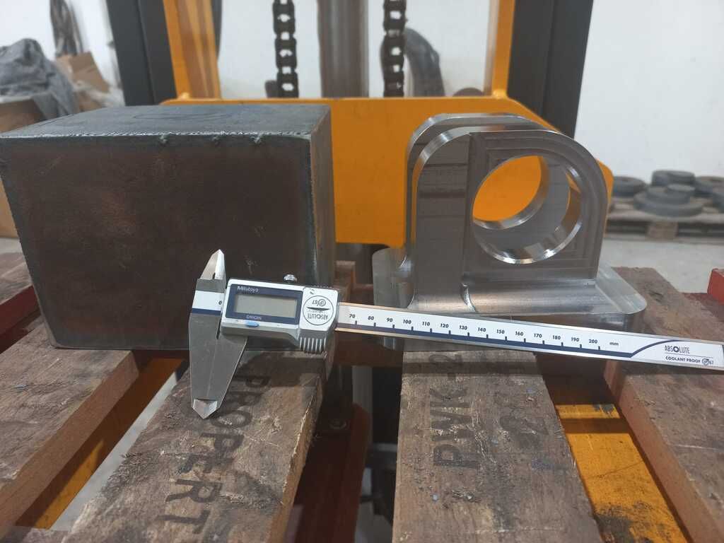 Un calibrador digital está sobre una paleta de madera al lado de un trozo de metal.