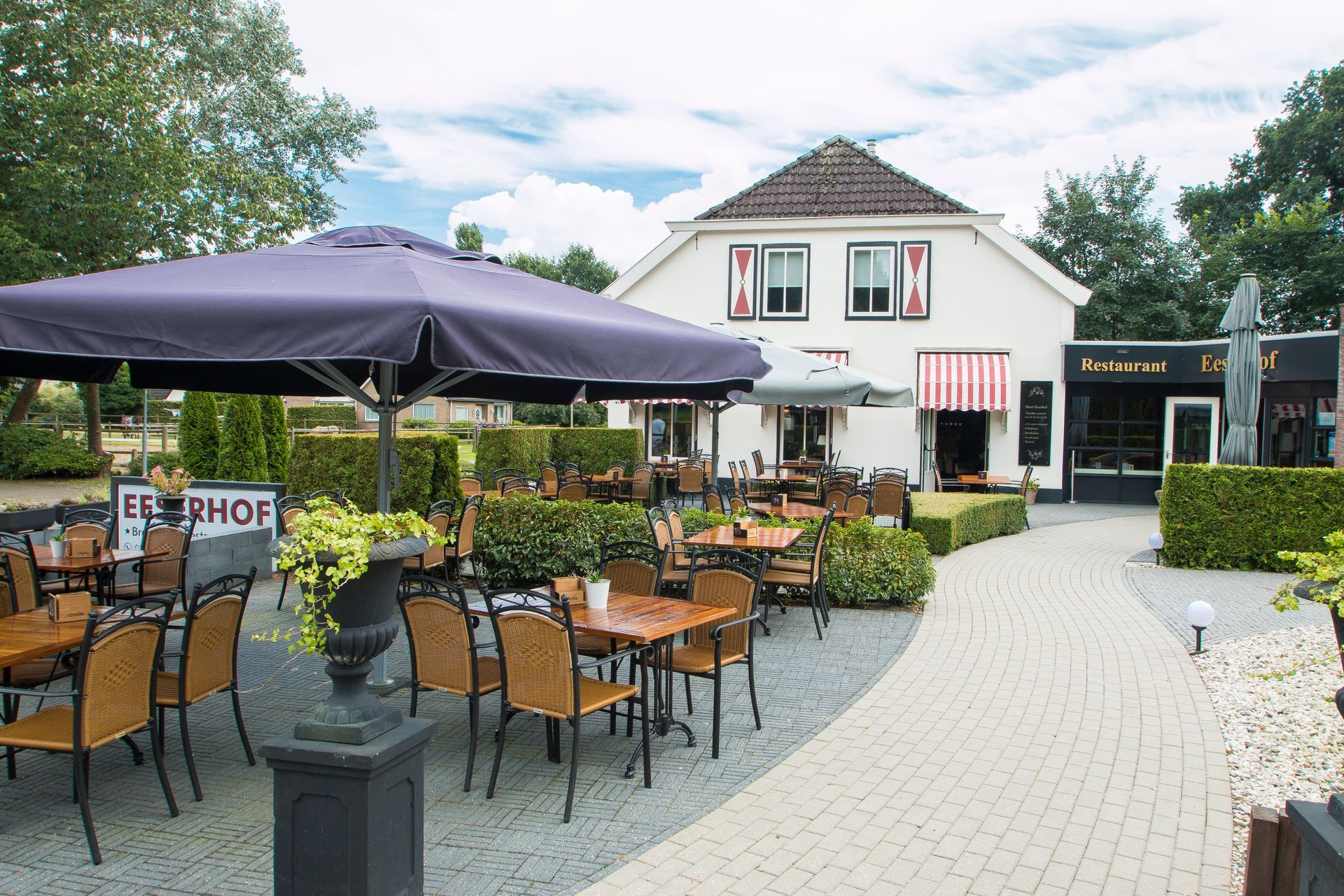 Wit huis met roodgestreepte luifels naast bloeiende paarse hortensia's