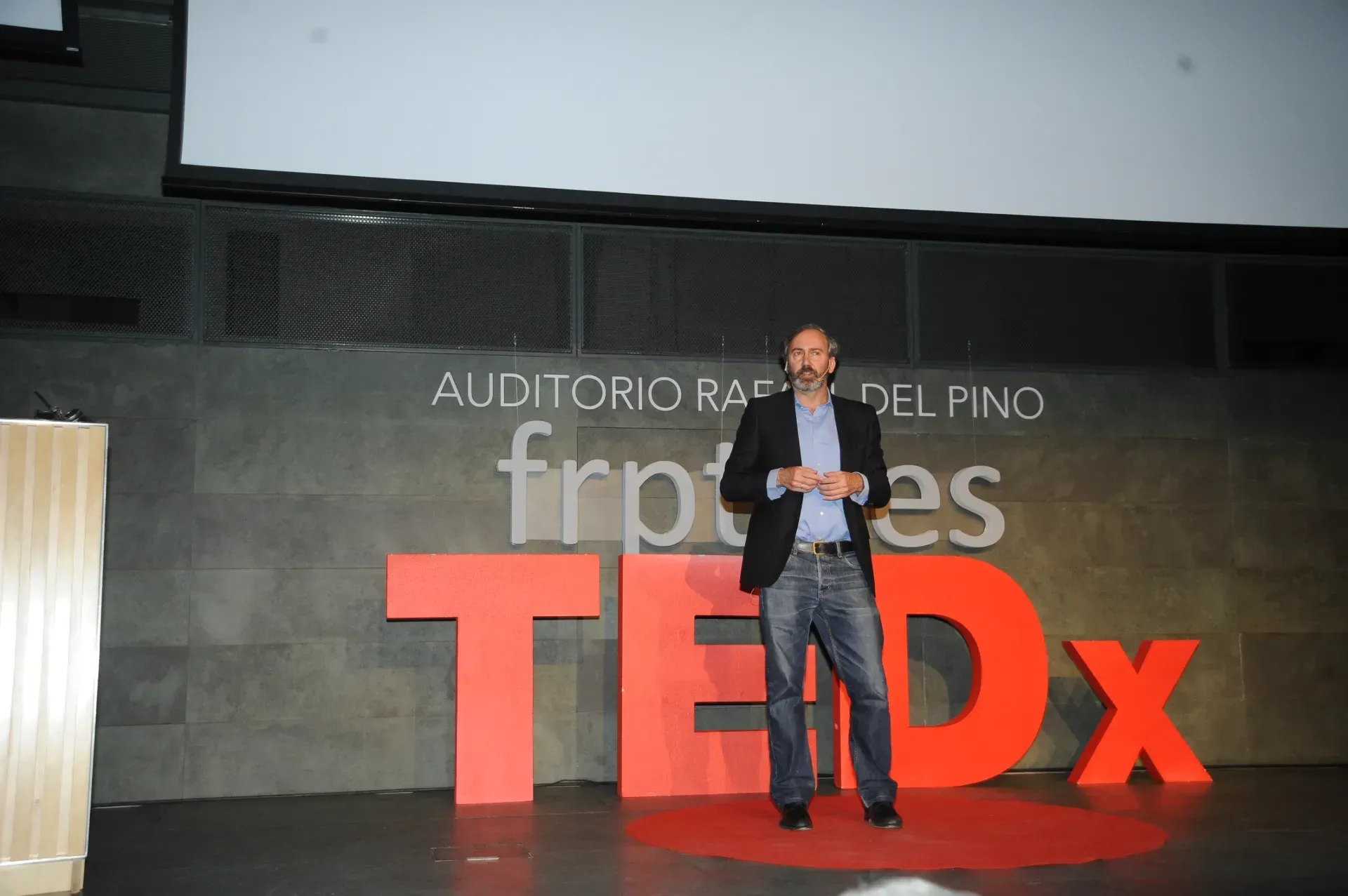 Un hombre está parado frente a un cartel de TEDX.