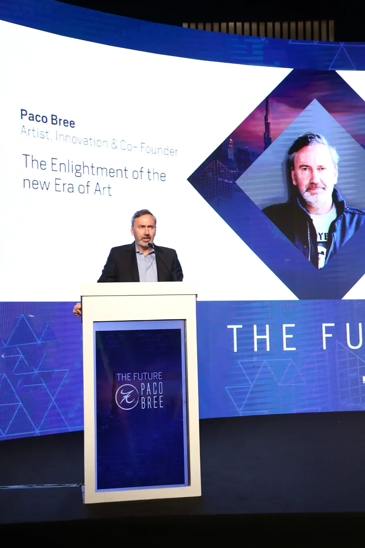 Un hombre está de pie en un podio frente a una pantalla que dice el futuro.