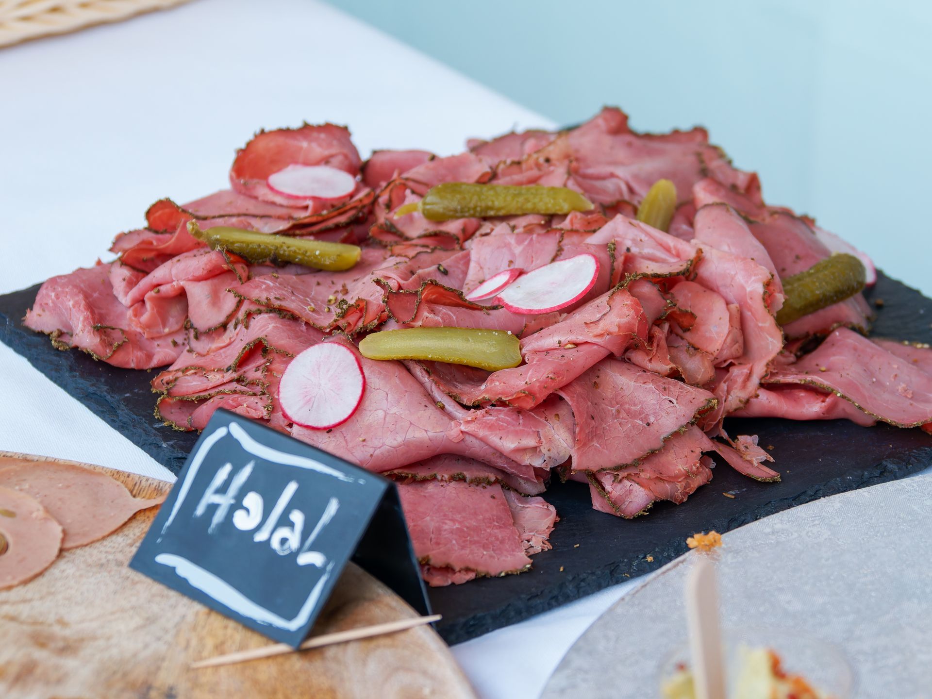 Tranches de rôti de bœuf avec cornichons et radis sur un plat en ardoise portant la mention halal.