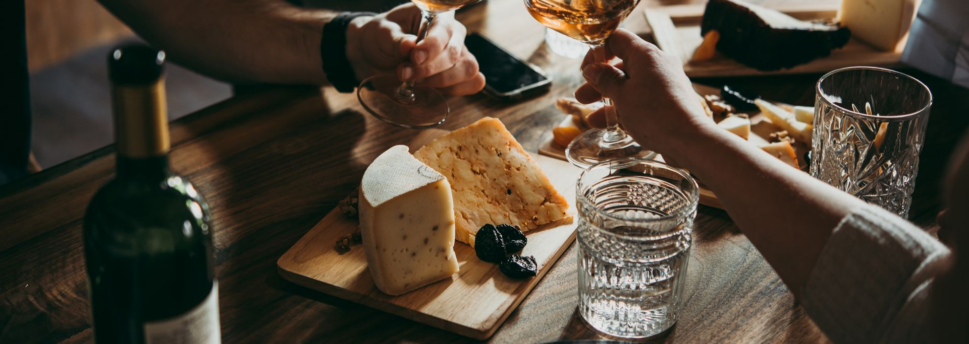 Des personnes trinquent avec du vin, en dégustant une planche de charcuterie avec du fromage, des olives et du pain.