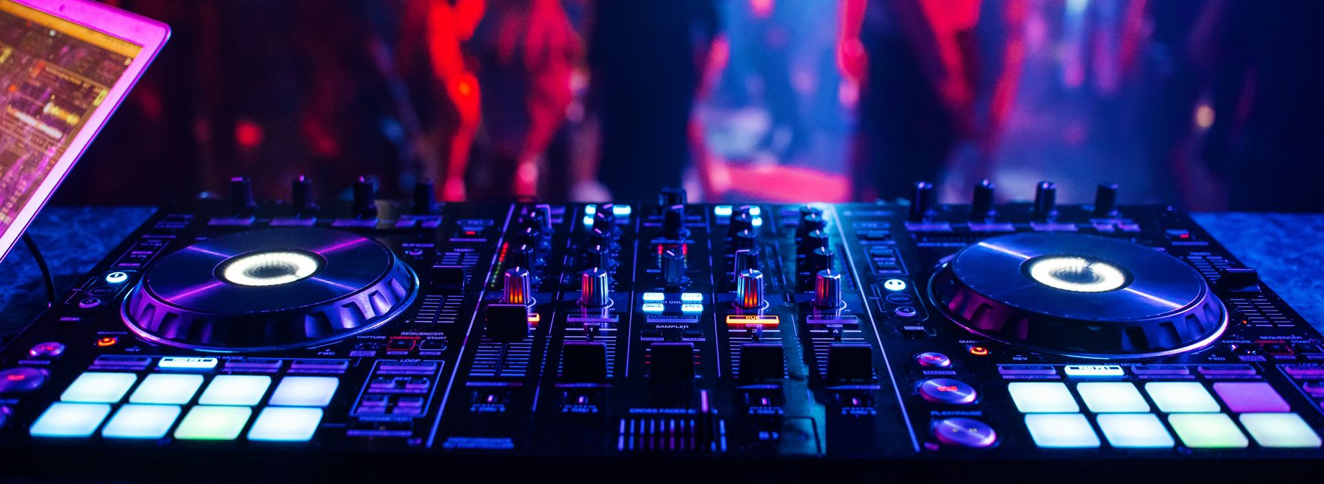 Une table de mixage de DJ dans une boîte de nuit, avec des lumières colorées et une foule en arrière-plan.