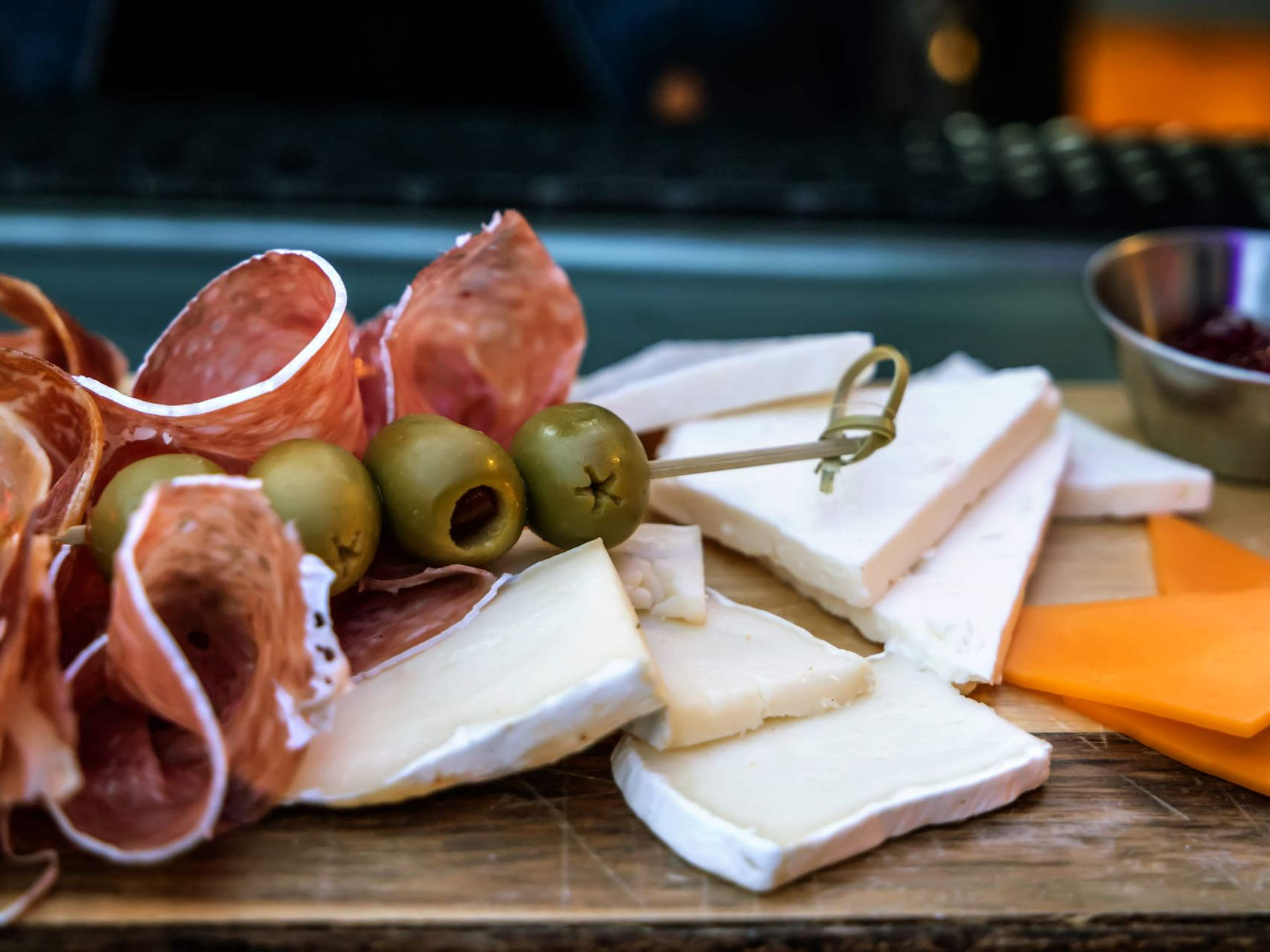 Planche de charcuterie avec salami, olives, fromages variés et assortiment de condiments.