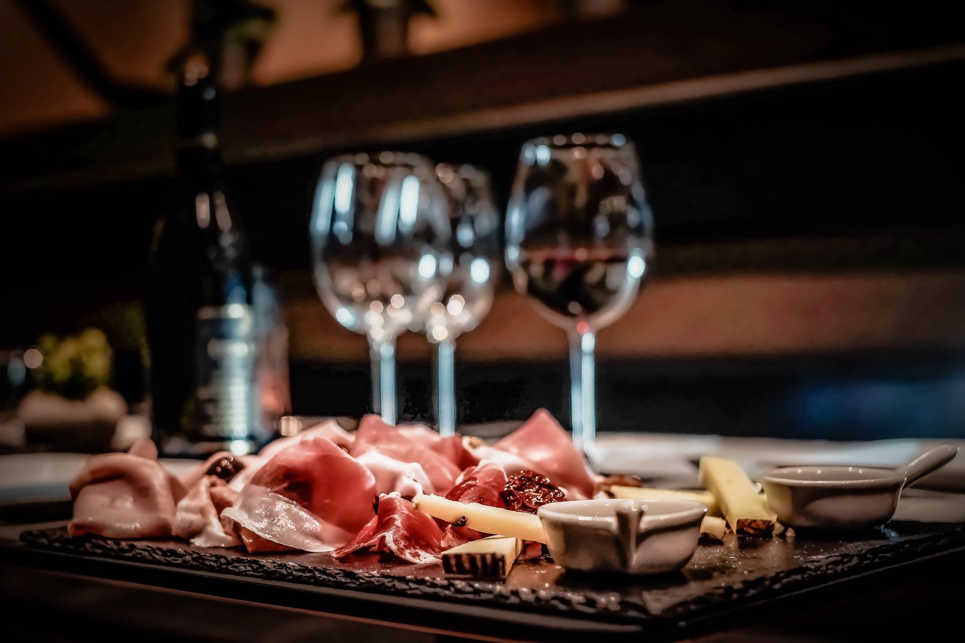 Planche de charcuterie avec prosciutto, fromage et figues, accompagnée de verres à vin et d'une bouteille, dans une ambiance tamisée.