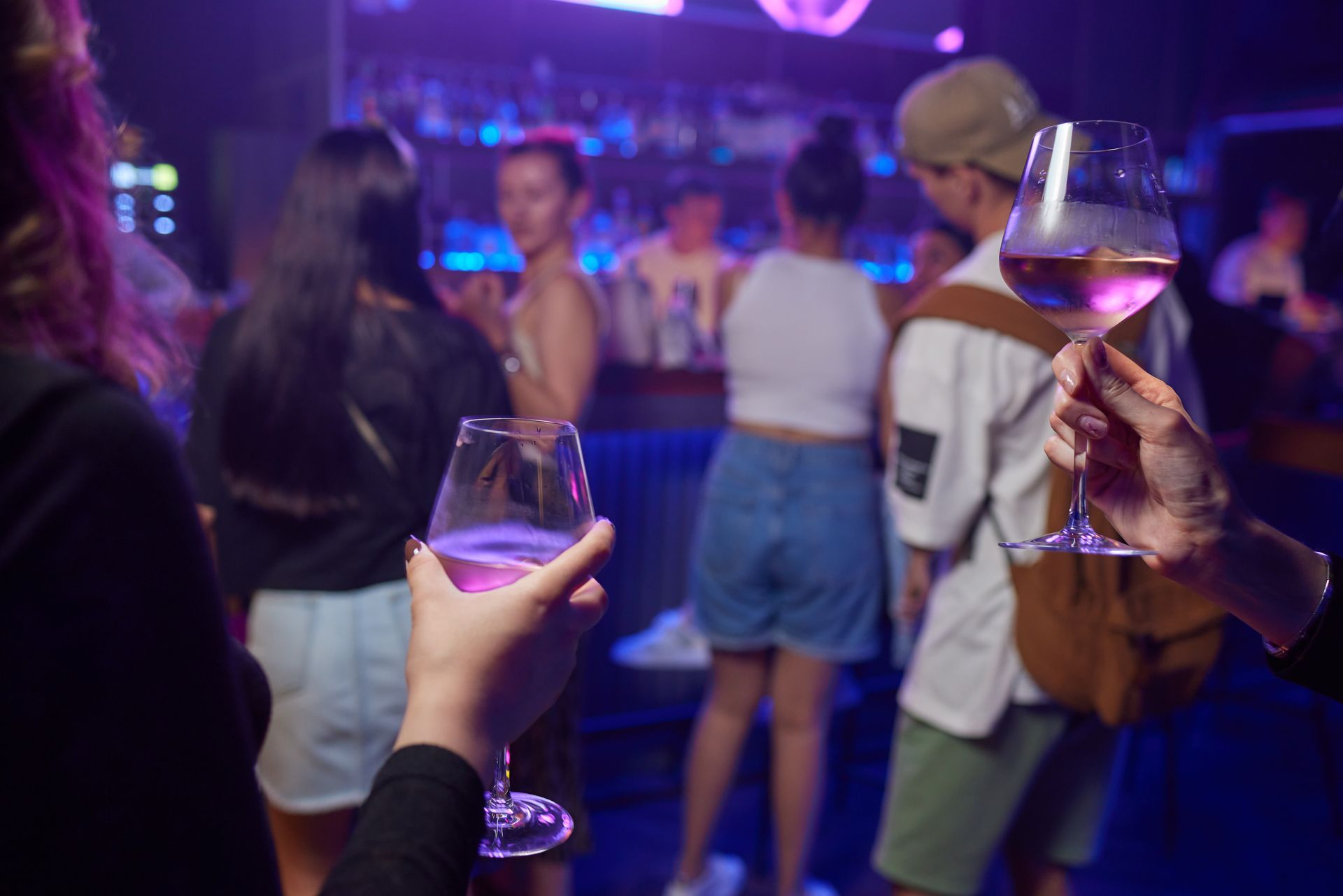 Des personnes attablées à un bar, verres à vin à la main, sous des lumières bleu et violet.