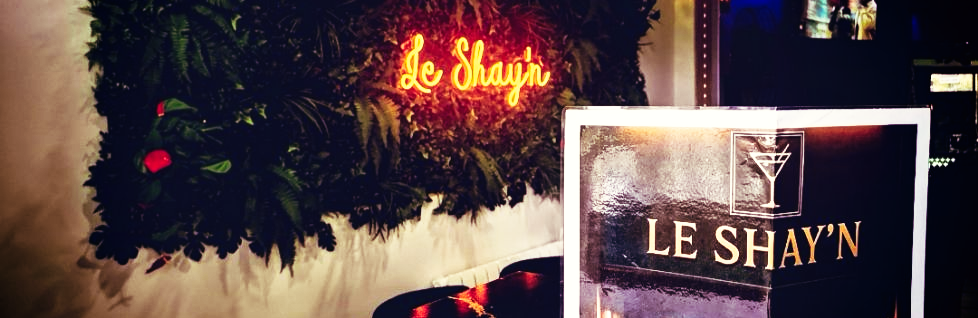 Enseigne lumineuse au-dessus d'un mur végétal, avec une carte des consommations, posée devant.