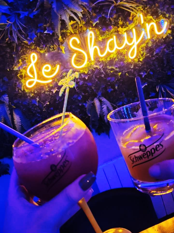 Deux cocktails présentés sous une enseigne lumineuse, dans un bar.