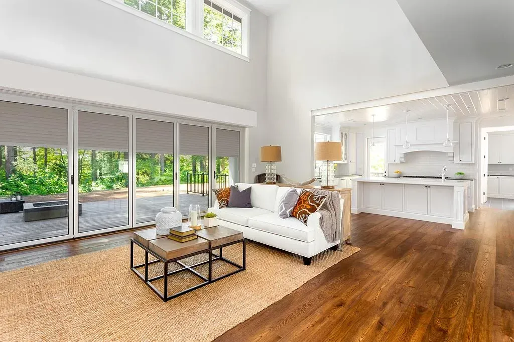 Salon spacieux avec canapé blanc, parquet et portes vitrées donnant sur un patio.