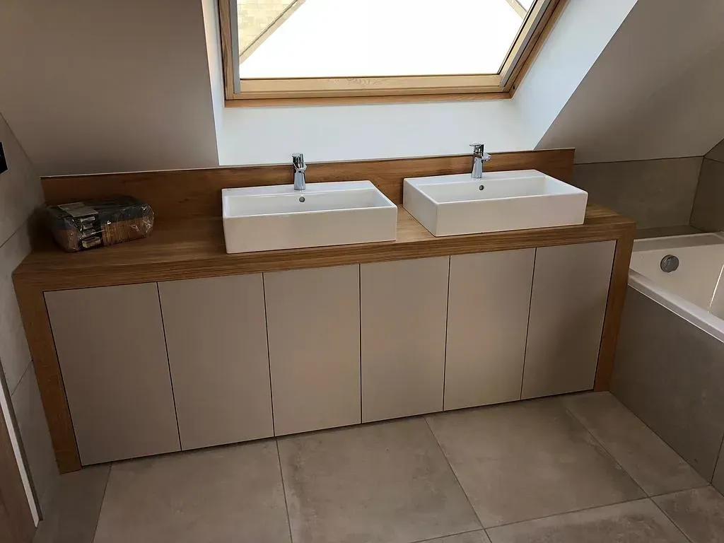 Meuble-lavabo avec deux lavabos blancs sur un comptoir en bois, des armoires blanches et un puits de lumière.