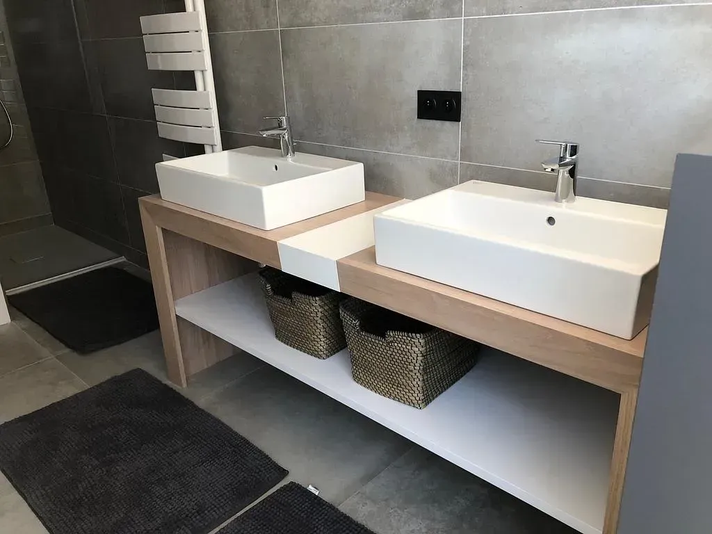 Meuble-lavabo avec deux lavabos blancs, cadre en bois et paniers en osier.
