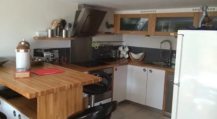 Cuisine avec îlot en bois, armoires blanches, électroménagers en acier inoxydable et dosseret gris.