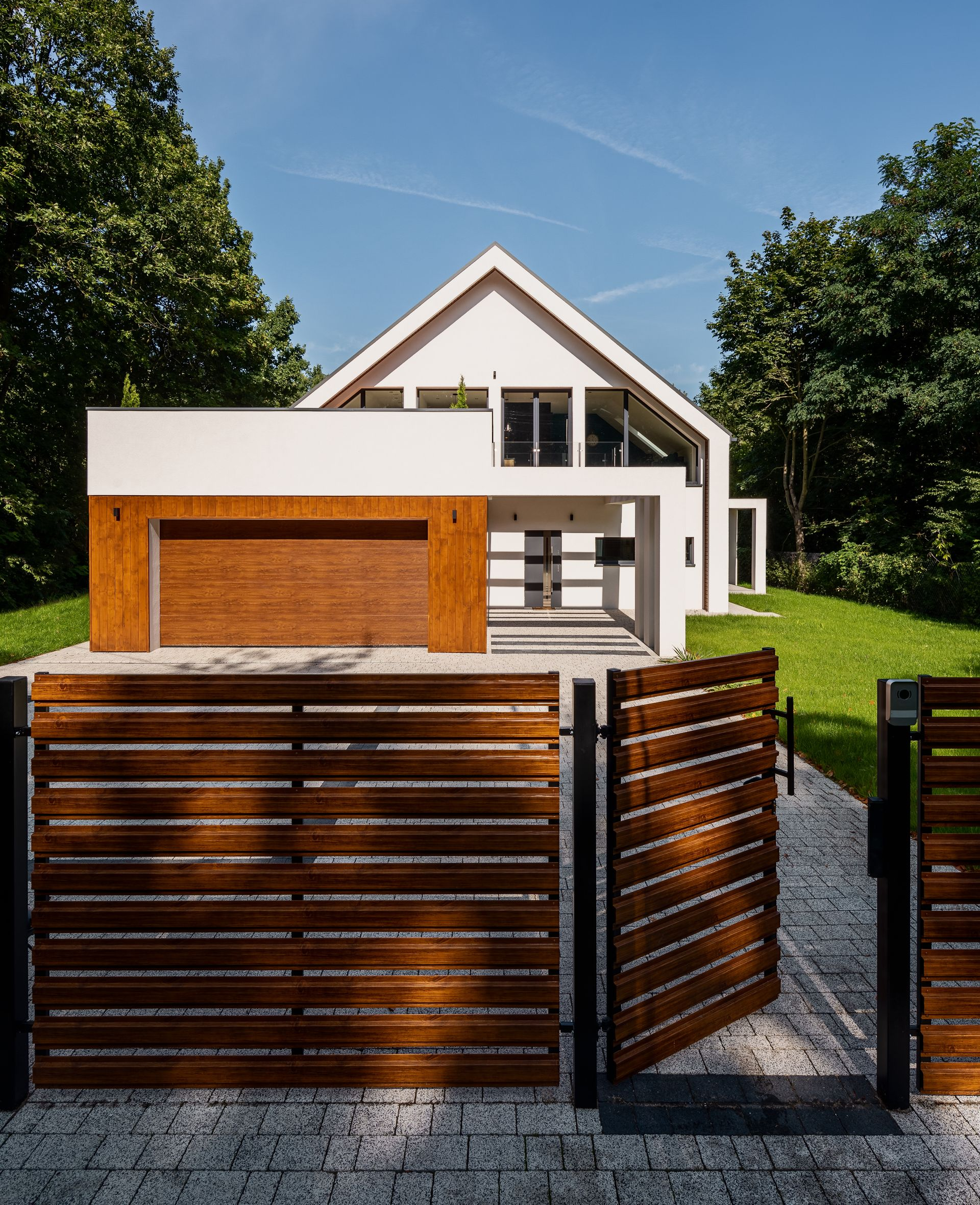 Maison blanche moderne avec porte de garage et clôture en bois ; ciel bleu.