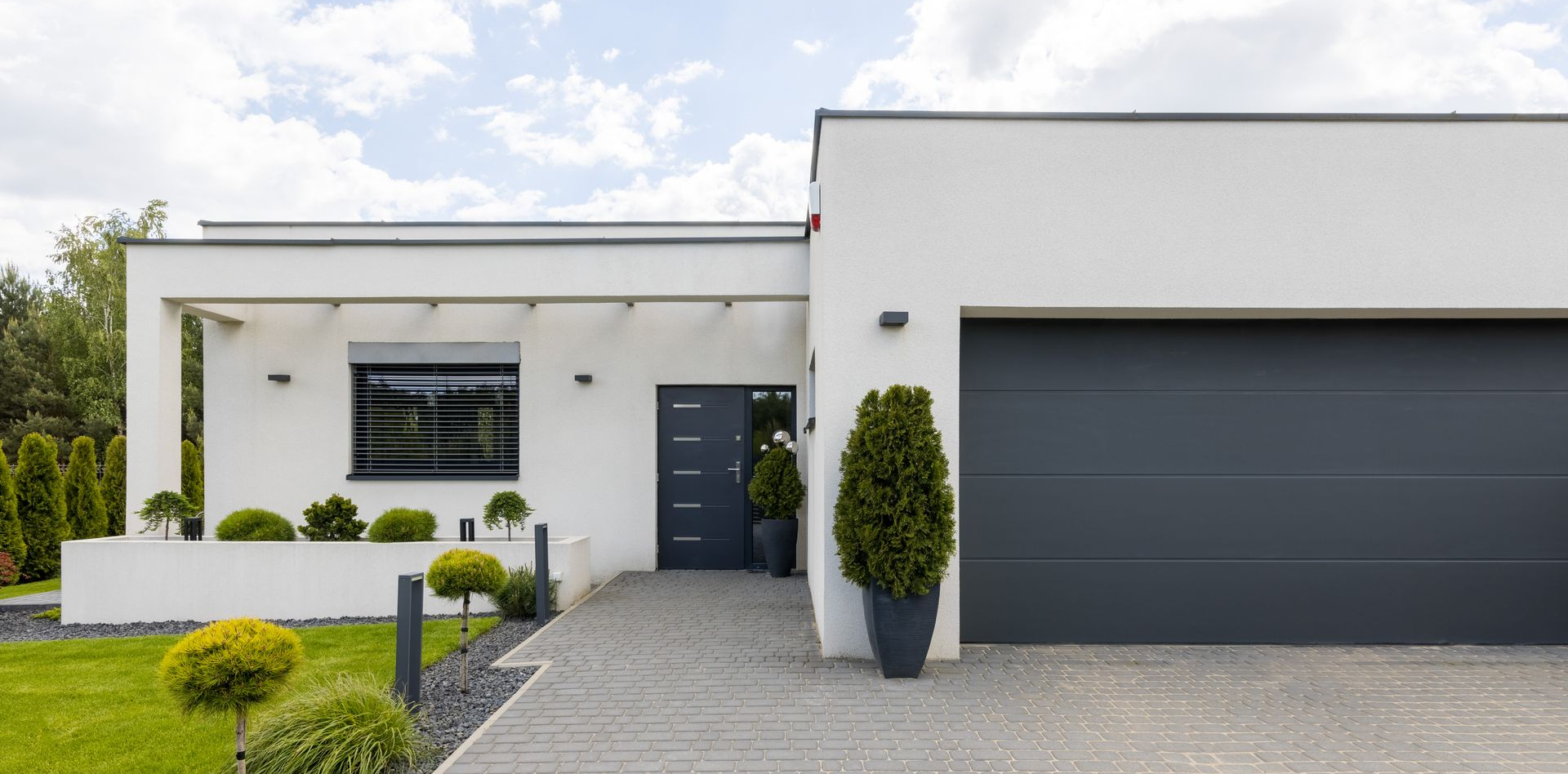 Maison blanche moderne avec une porte de garage grise et une allée en pierre.