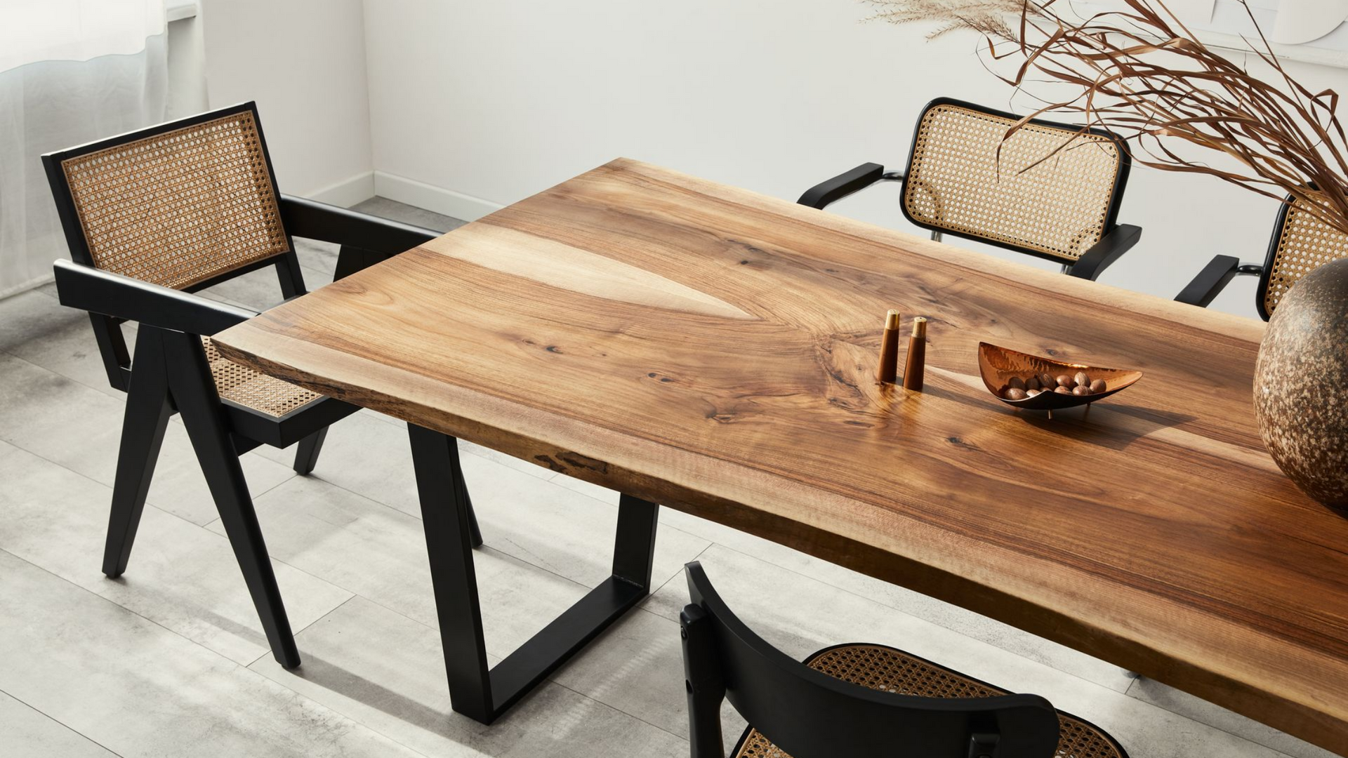 Table à manger en bois avec chaises noires, bol en cuivre et vase avec branches.