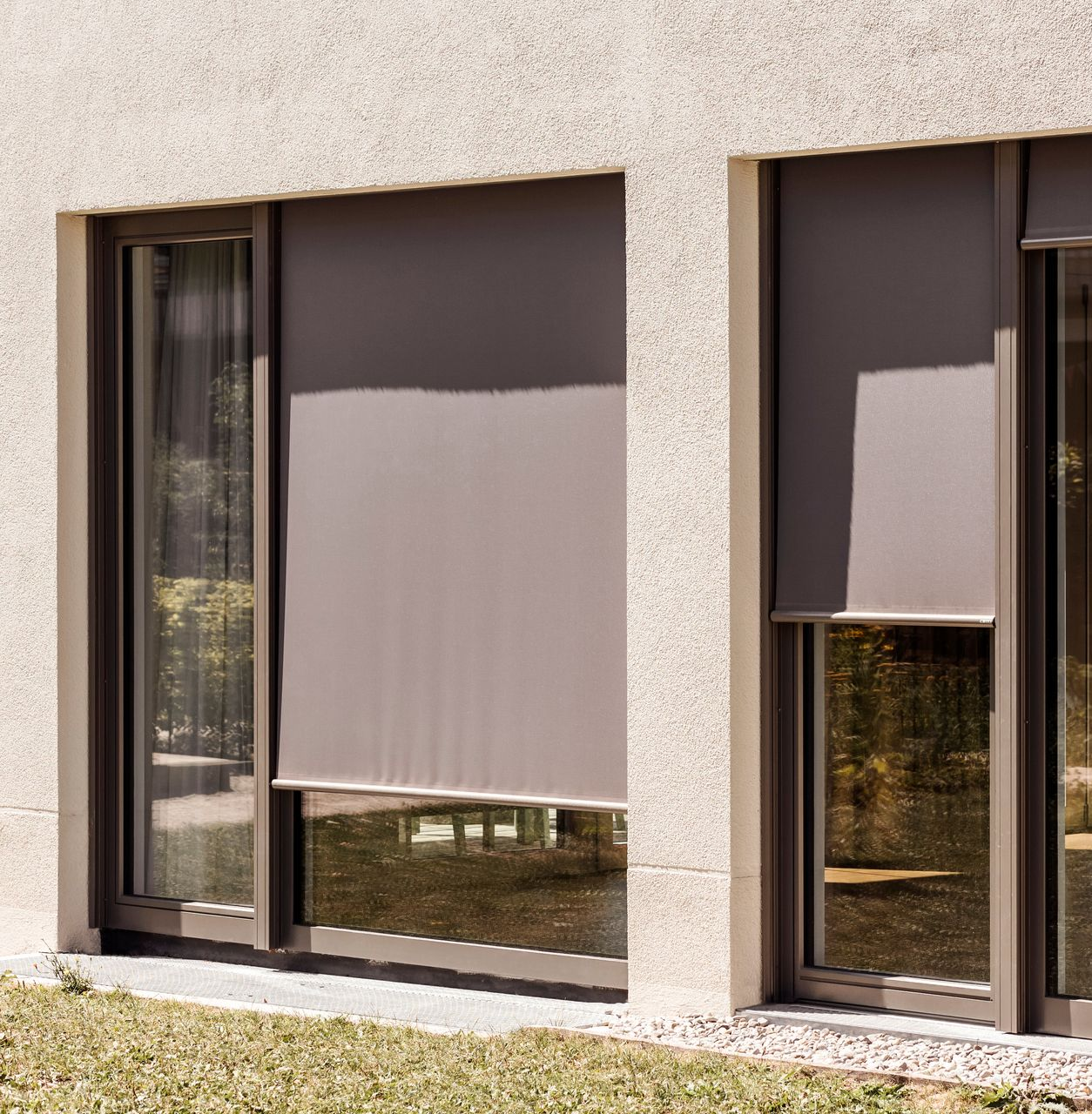Deux fenêtres avec des stores enrouleurs marron abaissés dans un bâtiment à l'extérieur de couleur claire.