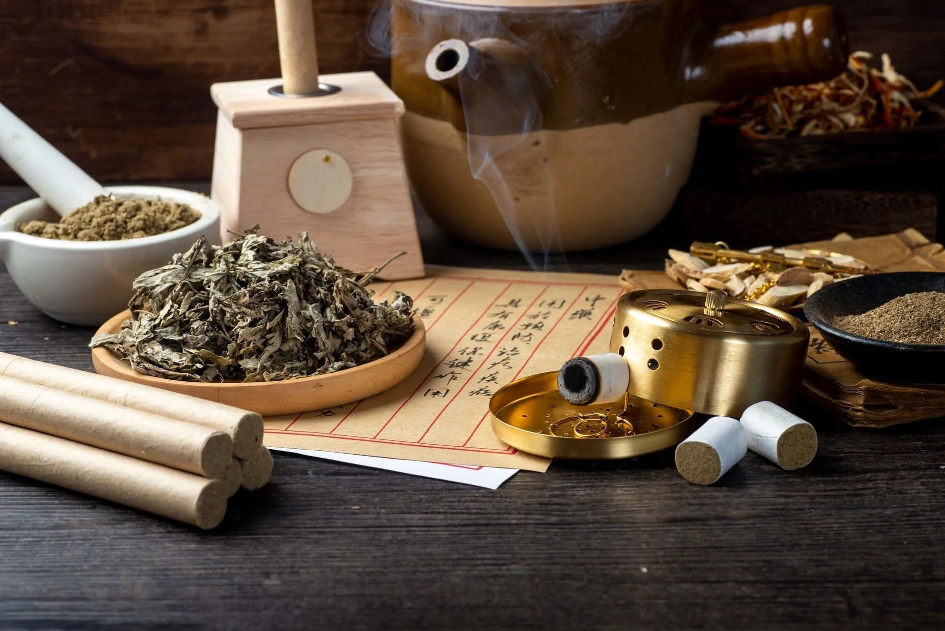 Traditionelles Teeservice mit losem Tee, Holzutensilien und einer braunen Teekanne auf einem dunklen Tisch