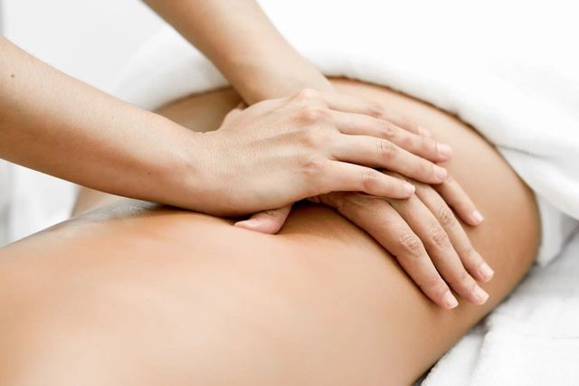 Hände massieren den unteren Rücken einer Person auf einem mit einem weissen Handtuch bedeckten Tisch.