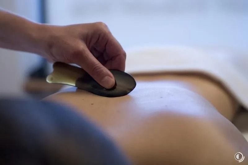 Hand benutzt einen Massagestein auf dem nackten Rücken einer Person während einer Spa-Behandlung