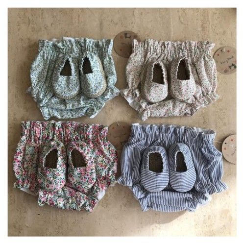 Cuatro pares de zapatos de bebé con pantalones bombachos estampados, cada uno de un color diferente: azul, beige, rosa y azul rayado.