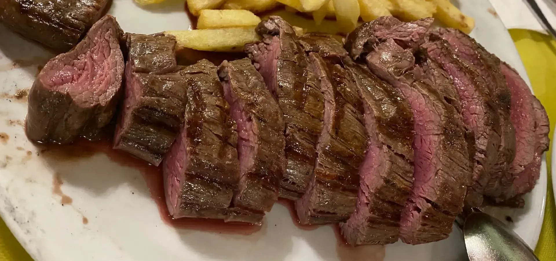 Filete rebanado con papas fritas en un plato blanco. La carne roja está al punto.