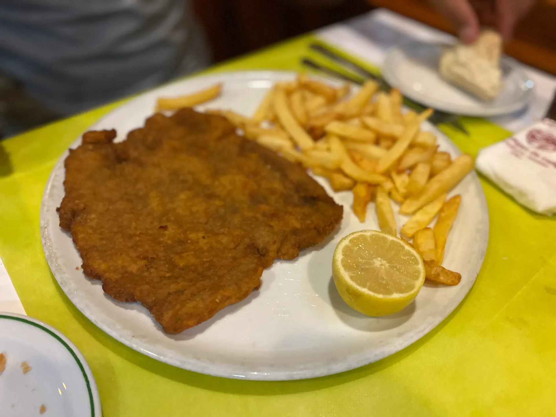 Escalope empanizado con patatas fritas y limón en un plato blanco.