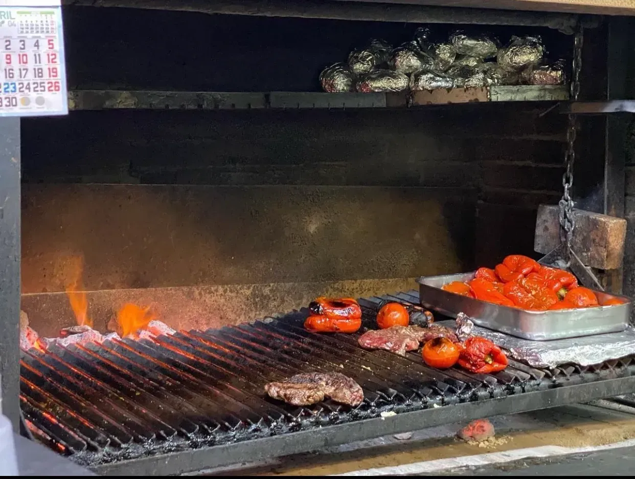 Una parrilla con filetes, tomates, pimientos y brasas brillantes en la cocina de un restaurante.